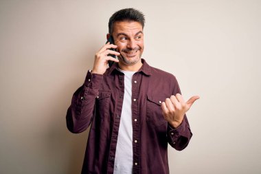 Genç yakışıklı bir adam beyaz arka planda akıllı telefondan konuşuyor ve gülümseyen bir yüzle baş parmağıyla işaret ediyor.
