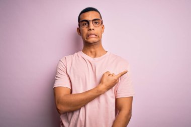 Yakışıklı Afro-Amerikalı adam pembe arka plan üzerinde günlük tişört ve gözlük takıyor. Endişeli, endişeli ve şaşırmış ifadesini bir kenara bırakıyor.