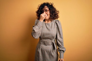 Güzel bir Arap iş kadını. Elbise ve gözlük takıyor. Sarı arka planda duruyor. Kokuşmuş ve iğrenç bir koku alıyor. Kötü kokuyor.