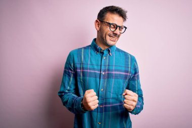 Sıradan gömlek ve gözlük takan yakışıklı genç adam başarı için heyecanlı kolları havada ve gözleri kapalı zaferi kutlarken gülümsüyor. Kazanan konsept.