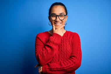 Mavi arka planda günlük süveter ve gözlük takan genç ve güzel Asyalı bir kadın çapraz kollar ve çeneyle gülümseyen kameraya kendinden emin bakıyor. Olumlu düşünüyorum..