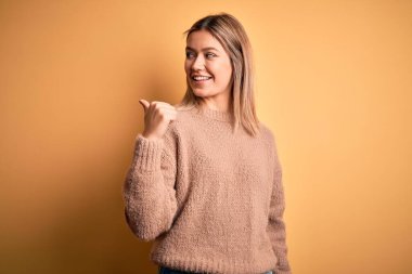 Sarıya boyanmış kahverengi süveter giyen genç ve güzel bir kadın. Mutlu yüzle gülümseyen ve başparmağıyla yan tarafı gösteren..