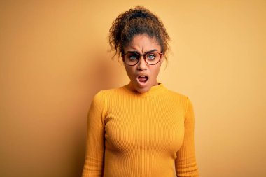 Sarı arka planda süveter ve gözlük takan Afro-Amerikan genç ve güzel bir kız. Şok suratlı, şüpheci, alaycı, ağzı açık ve şaşırmış görünüyor.