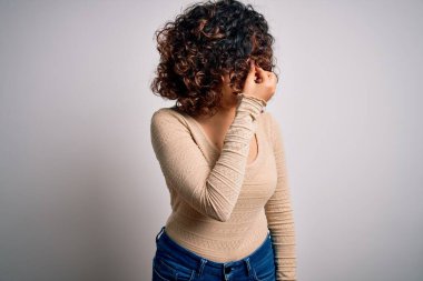 Genç, kıvırcık Arap bir kadın beyaz arka plan üzerine günlük tişört ve gözlük takıyor. Burnunu ve gözlerini ovuşturup yorgunluk ve baş ağrısı çekiyor. Stres ve hüsran kavramı.