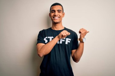 Beyaz arkaplan üzerine üniforma giymiş genç, Afro-Amerikan bir işçi. Arka tarafı işaret ediyor. El ve baş parmakları havada, kendinden emin.