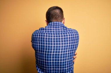 Sarışın, sakallı ve mavi gözlü genç bir işadamı sarı arka planda tişört giyip mutlu ve pozitif bir şekilde sarılıyor. Sevgi ve özgüven.