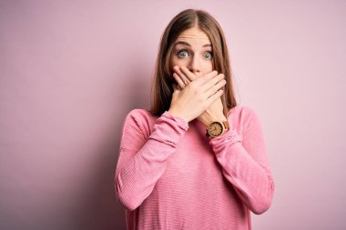 İzole edilmiş pembe arka plan üzerine gündelik kazak giyen genç, güzel, kızıl saçlı bir kadın yanlışlıkla ağzı ellerle kapatmış. Gizli konsept.