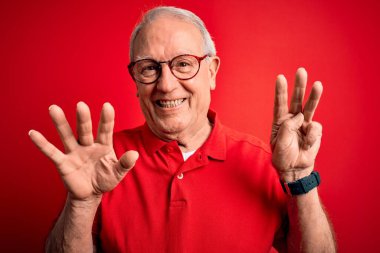 Gri saçlı, gözlüklü, kırmızı arka planda rahat tişörtlü, 8 numaralı parmaklarıyla işaret eden, kendinden emin ve mutlu gülümseyen son sınıf öğrencisi..