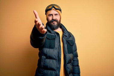 Sakallı, kar maskeli, kar maskeli ve kayak gözlüklü yakışıklı kayakçı dostça el sıkışma ve hoş geldin demek için gülümsüyor. Başarılı bir iş..