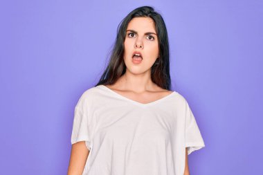 Genç, güzel, esmer bir kadın mor arka plan üzerine günlük beyaz tişört giyiyor. Şok suratlı, şüpheci ve alaycı görünüyor, ağzı açık bir şekilde şaşırmış.