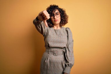 Güzel Arap iş kadını elbise ve gözlük takıyor sarı arka planda dikiliyor mutsuz ve kızgın görünüyor reddediliyor ve olumsuz jestler yapıyor. Kötü ifade.