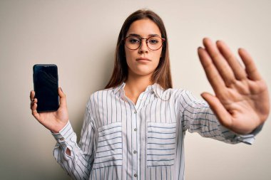 Genç, güzel, esmer bir kadın elinde akıllı telefonuyla beyaz arka planda ekranı gösteriyor. Eli açık, dur işareti yapıyor. Ciddi ve kendinden emin bir ifadeyle.