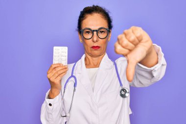 Orta yaşlı, uzman doktor kadın elinde kızgın yüzlü ilaç hapları var. Negatif işaretler baş parmakları aşağıda, reddedilme konsepti reddedildi.