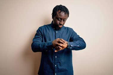 Beyaz arka plan üzerinde duran, rahat ve kendinden emin genç, Afro-Amerikalı bir adam kol saatini kontrol ediyor.