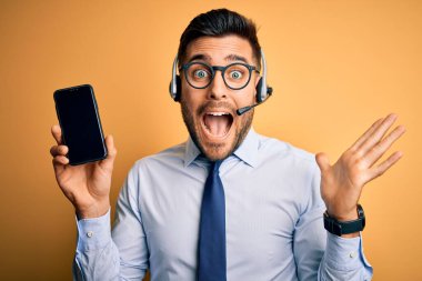 Çağrı merkezinden gelen müşteri hizmetleri kulaklığı takan iş adamı akıllı telefon ekranını çok mutlu ve heyecanlı gösteriyor. Kazanan ifade zaferi büyük bir gülümsemeyle kutluyor ve ellerini kaldırıyor.