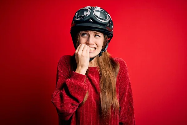 赤い背景に元ヘルメットを身に着けている若い美しい赤毛の元サイクリストの女性は 口の上で爪をかむ上で手でストレスと緊張しています 不安の問題 — ストック写真