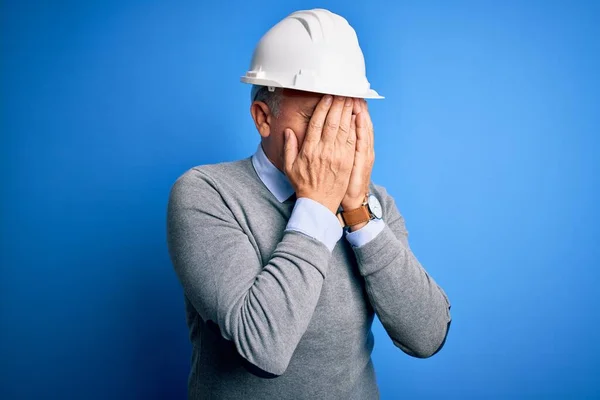 泣きながら手で顔を覆う悲しい表情で青の背景に安全ヘルメットを身に着けている中世のハンサムな白髪のエンジニアの男 うつ病の概念 — ストック写真
