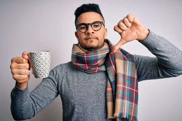 Young handsome man wearing scarf drinking mug of hot coffe over isolated white background with angry face, negative sign showing dislike with thumbs down, rejection concept