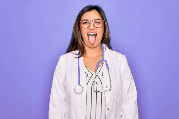 面白い表情で幸せ舌を突き出す紫色の背景に聴診器や医療用コートを身に着けている専門医の女性 感情概念 — ストック写真