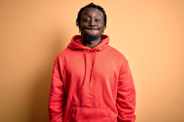 Young african american sporty man wearing sweatshirt with hoodie over yellow background puffing cheeks with funny face. Mouth inflated with air, crazy expression.