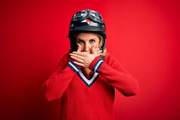 中世の美しいブロンドのオートバイの女性は 間違いのために手で口をカバーショックを受けた赤い背景に元ヘルメットを身に着けています 秘密概念 — ストック写真