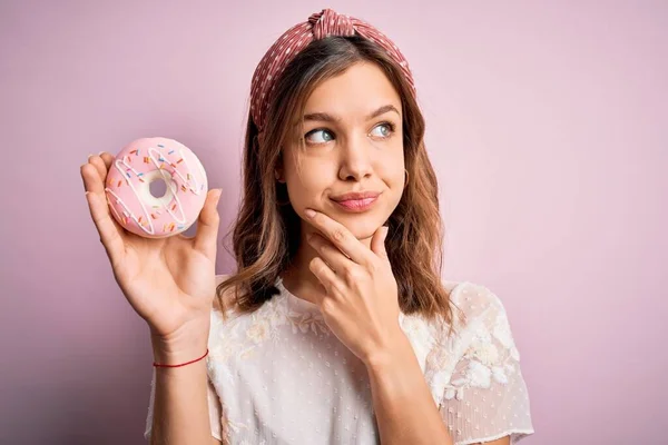若いですブロンド女の子食べる甘いですベーカリーシュガードーナツ以上ピンク隔離された背景深刻な顔考え約質問 非常に混乱したアイデア — ストック写真