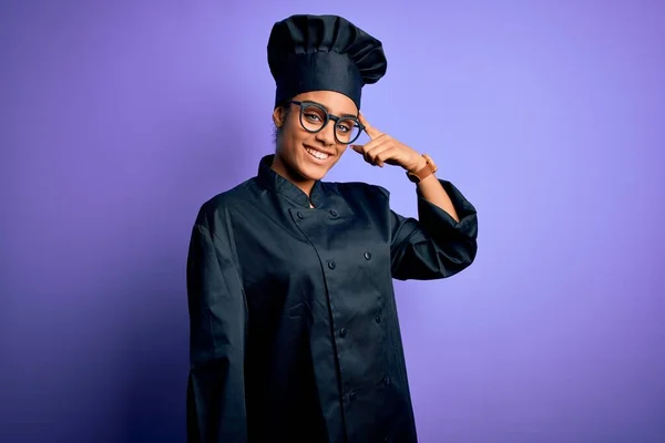 Young african american chef girl wearing cooker uniform and hat over purple background Smiling pointing to head with one finger, great idea or thought, good memory