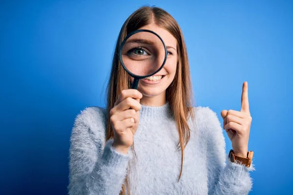 Jovem Bela Mulher Detetive Ruiva Usando Lupa Sobre Fundo Azul — Fotografia de Stock