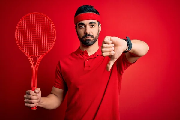年轻英俊的有胡子的运动员打网球时 用球拍盖住红底 满脸怒容 负面信号表示不喜欢大拇指朝下 拒绝的概念 — 图库照片