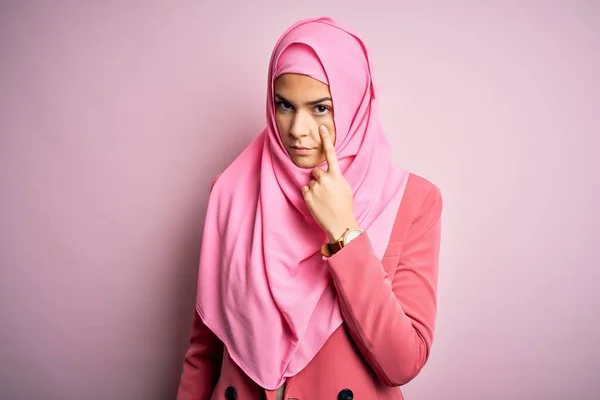 穿着穆斯林头巾站在孤立的粉色背景上的年轻漂亮的女孩指着你的眼睛看着你的手势 怀疑的表情 — 图库照片
