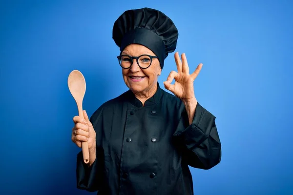 高级美丽的白发女厨师身穿炊具制服 头戴木制勺子帽 手握手签 象征非凡 — 图库照片