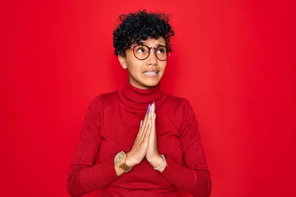 Young beautiful african american afro woman wearing turtleneck sweater and glasses begging and praying with hands together with hope expression on face very emotional and worried. Begging.