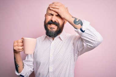 Sakallı, dövmeli, pembe arka planda kahve içen yakışıklı kel bir adam. Elleri başının üstünde, utanç ve şaşkınlık dolu, sinirli ve hayal kırıklığına uğramış. Hata için korku ve üzüntü.