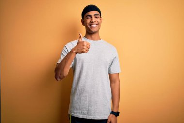 Sarı arka planda spor giyerek spor yapan yakışıklı Afro-Amerikan sporcusu elle mutlu bir jest yapıyor. Kameraya bakıp başarıyı gösteren ifade onaylanıyor.