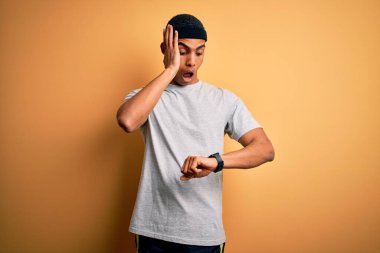 Yakışıklı Afro-Amerikan sporcusu sarı arka planda spor giysisi giyiyor. Endişeli saate bakıyor, geç kalmaktan korkuyor.