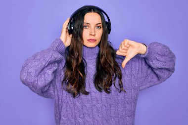 Mavi gözlü genç bir kadın müzik dinliyor ve dans ediyor. Kızgın yüzlü kulaklıklar takıyor. Negatif işaretler baş parmakları aşağıda, reddedilme konsepti var.