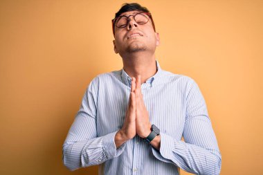 Sarı arka planda inek gözlüğü takan genç, yakışıklı İspanyol iş adamı elleri bağlı yalvarıyor ve dua ediyor. Yüzünde umut ifadesi var. Çok duygusal ve endişeli. Yalvarıyorum..