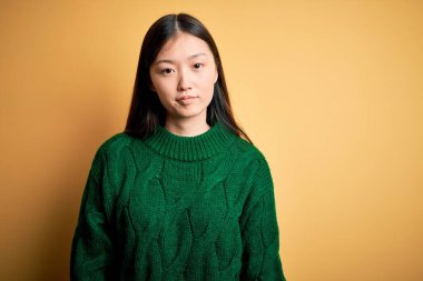 Sarı arka plan üzerine yeşil kazak giyen genç, güzel Asyalı kadın uykulu ve yorgun görünüyor, yorgunluktan ve akşamdan kalmalıktan yorgun, sabahları tembel gözler..