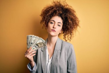 Kıvırcık saçlı ve piercingli genç bir kadın. Elinde dolar banknotları var. Zeki bir yüz ifadesi var.