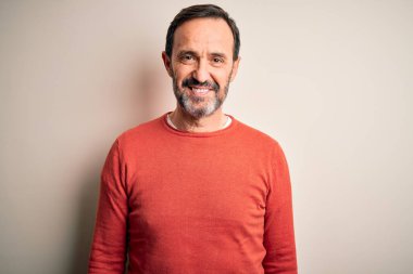 Orta yaşlı, turuncu bir süveter giyen, mutlu ve havalı bir gülümseme ile izole edilmiş beyaz arka planda duran, orta yaşlı bir adam. Şanslı kişi..