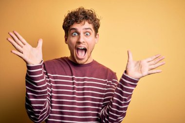 Sarışın, kıvırcık saçlı, sıradan çizgili süveter giyen genç, çılgın ve başarıyı kolları açık, gözleri açık ve heyecanlı bir şekilde kutlayan yakışıklı bir adam. Kazanan konsept