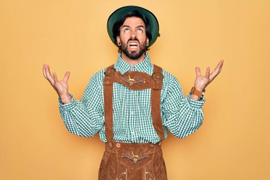 Almanya festivali için geleneksel Alman Ekim Festivali kıyafeti giyen genç yakışıklı adam çılgın ve kızgın bir şekilde bağırıyor ve agresif bir ifade ve kolla bağırıyor. Hayal kırıklığı konsepti.