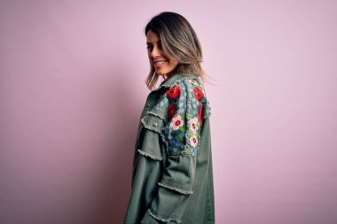 Moda kıyafetleri giyen genç ve güzel bir kadın. Manken, sokak tarzı giyiniyor. Pembe arka planda dikiliyor.