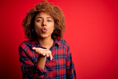 Kıvırcık saçlı, rahat gömlekli genç, Afro-Amerikan bir kadın kameraya bakıyor ve havada bir öpücük savuruyor. Güzel ve seksi. Aşk ifadesi.