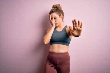 Genç ve güzel sarışın sporcu kadın spor yapıyor. Pembe arka plan üzerine spor giysisi giyip gözleri ellerle kaplıyor ve üzgün ve korku ifadeleriyle jestleri durduruyor. Utanç verici ve olumsuz bir kavram..