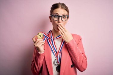 Genç, güzel, kızıl saçlı bir kadın, izole edilmiş kırmızı arka planda madalyalar takıyor. Ağzı kapalı, utancından ağzı açık, korkusunun dışa vurumu, sessizlikten korkması, gizli konsept.