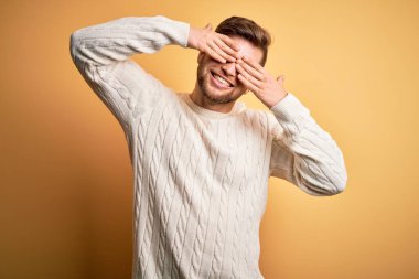 Sarışın, sakallı ve mavi gözlü genç adam sarı arka planda beyaz süveter giyiyordu. Gözleri neşeli ve komik gülümseyerek kaplıyordu. Kör kavram.