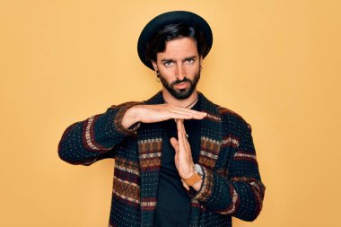 Genç, yakışıklı, bohem, hippi tarzı ve bohem şapkalı bir adam. El kol hareketleri yapıyor, hayal kırıklığına uğramış ve ciddi bir yüz ifadesi var.