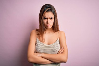 Genç ve güzel esmer kız, pembe arka plan kuşkucu ve gergin izole edilmiş, kollarını kavuşturmuş, tasvip etmeyen bir yüz ifadesi üzerine sıradan çizgili tişört giyiyor. Negatif kişi.