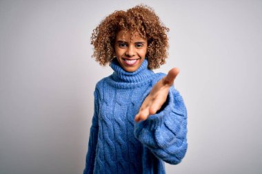 Beyaz arka plan üzerine balıkçı yaka kazak giyen güzel Afro-Amerikan kadın gülümseyen avuç içi yardım ve kabullenme eli uzatıyor..